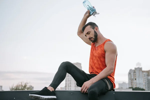 Apuesto deportista verter agua de botella en la cabeza en el techo - foto de stock