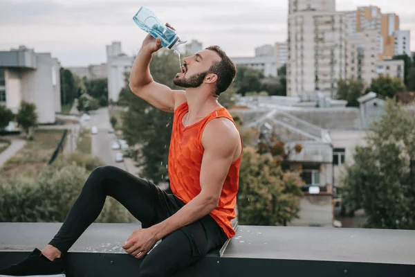 Apuesto deportista beber agua en el techo - foto de stock