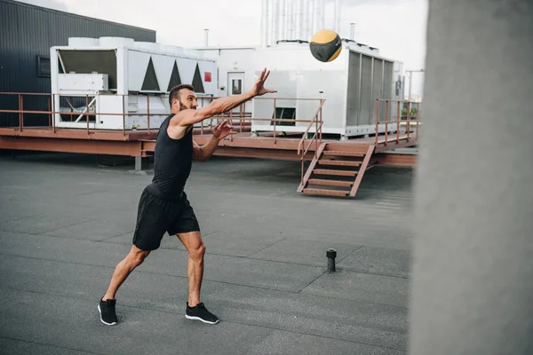 Beau sportif attrapant boule de médecine sur le toit — Photo de stock