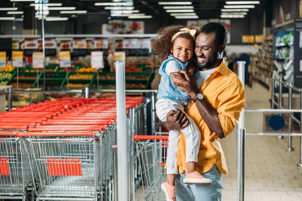 Happy african american man embracing and holding little daughter in grocery store — Stock Photo