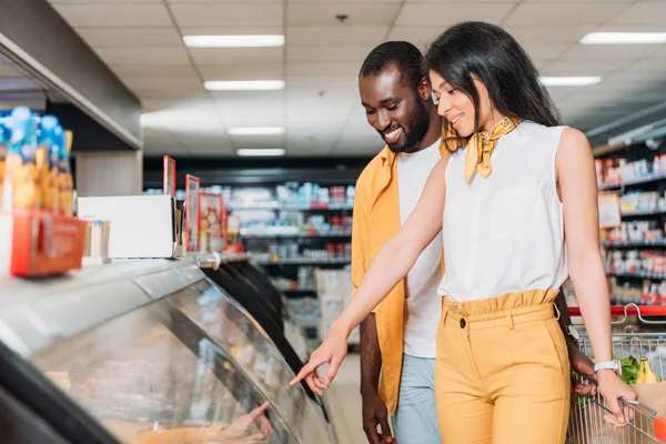 Atractiva mujer afroamericana señalando en escaparate en tienda de comestibles - foto de stock