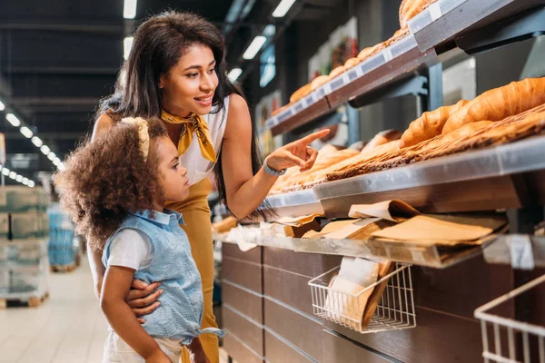 Африканская американка, указывающая пальцем на кондитерскую маленькую дочь в продуктовом магазине — стоковое фото