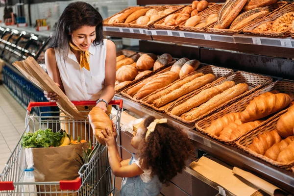 Femme afro-américaine souriante donnant du pain à un petit enfant dans un supermarché — Photo de stock