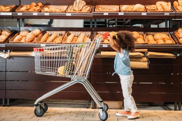 Вид збоку маленької афроамериканської дитини, що перевозить візок у супермаркеті — стокове фото