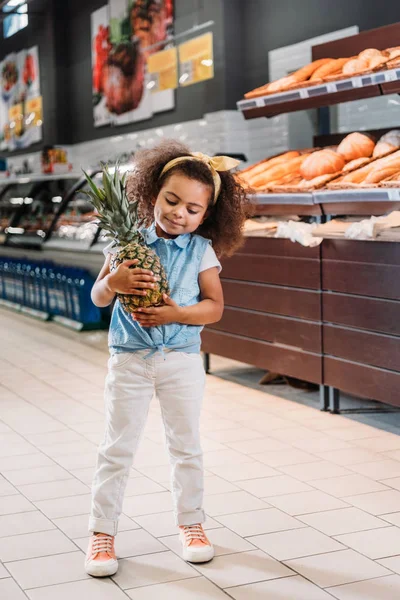 Little african american kid standing with pineapple in supermarket — Stock Photo