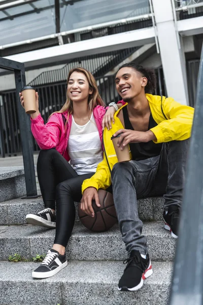 Couple multiethnique avec balle pour basket boire du café dans la rue de la ville — Photo de stock