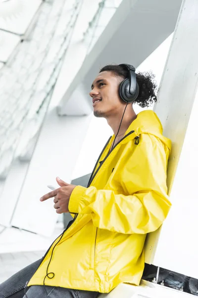 Selective focus of smiling mixed race man in headphones listening music with smartphone at city street — Stock Photo