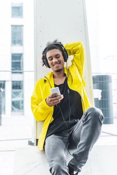 Uomo di razza mista sorridente in cuffia ascoltare musica con smartphone in città strada — Foto stock