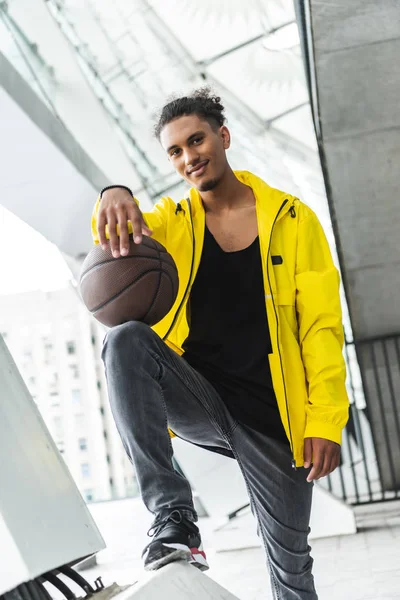 Молодой смешанной расы, стоящий с баскетбольным мячом и смотрящий в камеру на улице — стоковое фото