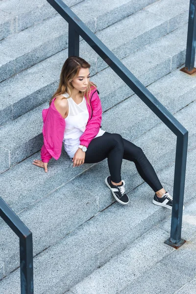 Alto ángulo vista de joven asiático mujer sentado en escaleras en urbano calle - foto de stock