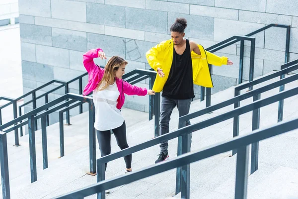 Vista de ángulo alto de la joven pareja multiétnica bailando en las escaleras en la calle urbana - foto de stock