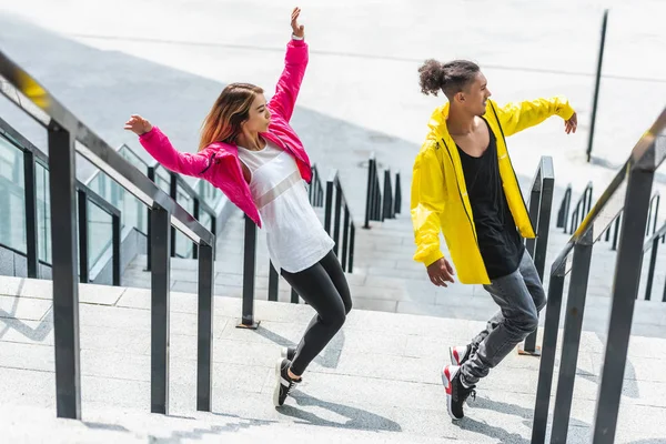 Vista de ángulo alto de la joven pareja multiétnica bailando en las escaleras en la calle urbana - foto de stock