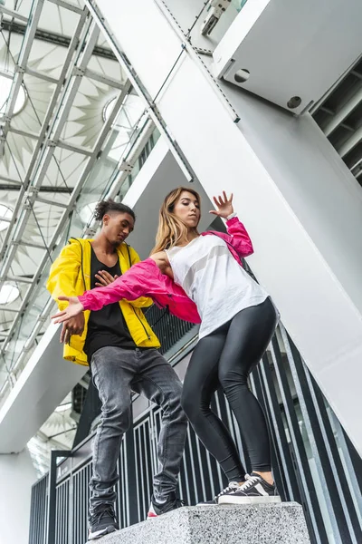 Vista de ángulo bajo de la pareja multiétnica de bailarines urbanos bailando en la calle - foto de stock