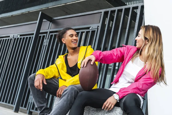 Junges, lächelndes multikulturelles Paar sitzt beim Rugbyball in der Stadt — Stockfoto