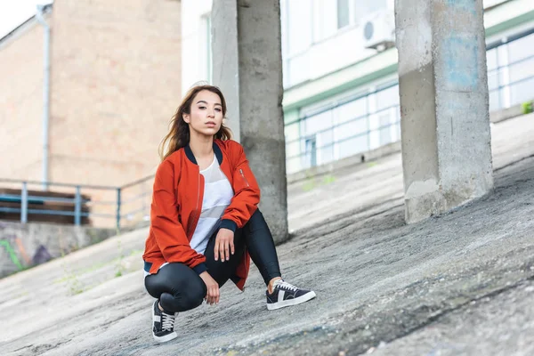 Selbstbewusste stilvolle asiatische Frau sitzt und schaut in die Kamera auf der städtischen Straße — Stockfoto