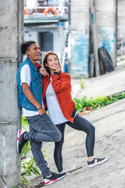 Foco seletivo de casal multiétnico sorridente em pé na rua urbana — Fotografia de Stock