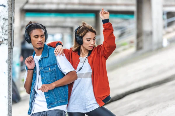 Стильна мультикультурна пара слухає музику з навушниками та танцює на міській вулиці — стокове фото