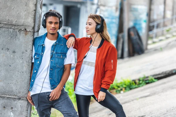 Stylish multicultural couple with headphones standing at city street — Stock Photo
