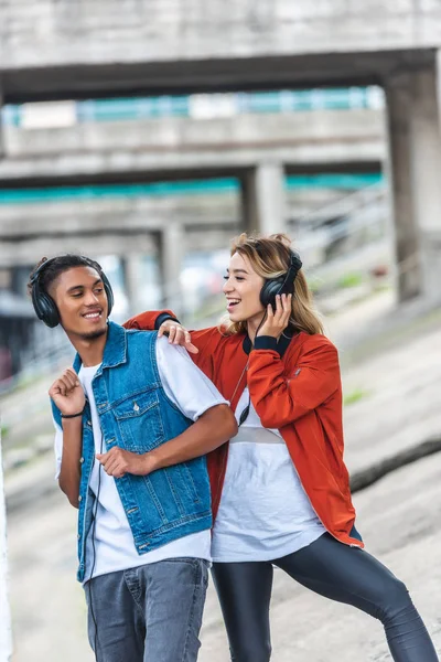 Feliz casal multicultural ouvir música com fones de ouvido e dançar na rua da cidade — Fotografia de Stock