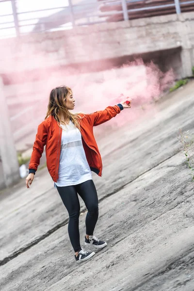 Attractive young asian woman holding red smoke bomb at city street — Stock Photo