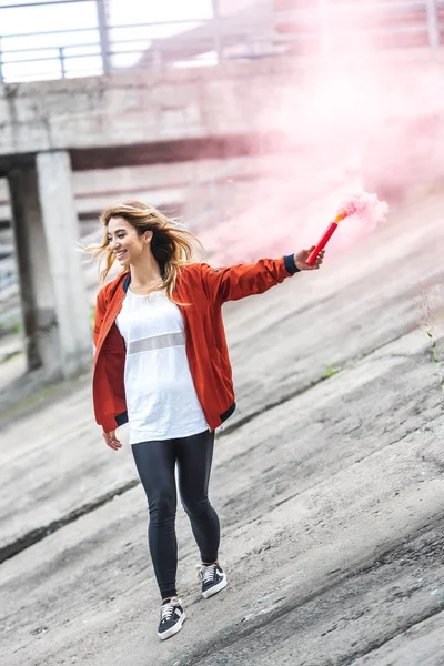 Stylish young asian woman holding red smoke bomb at city street — Stock Photo