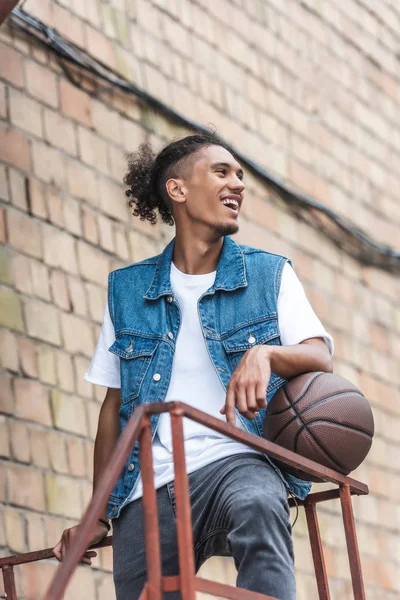 Felice giovane uomo gara mista in piedi con pallone da basket in strada — Foto stock