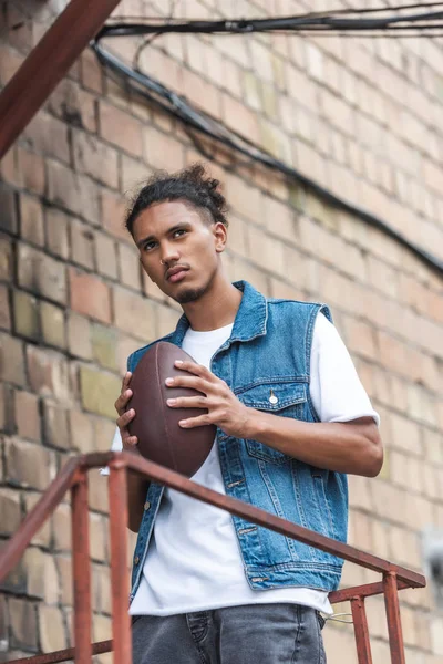 Serious mixed race man holding rugby ball at urban street — Stock Photo