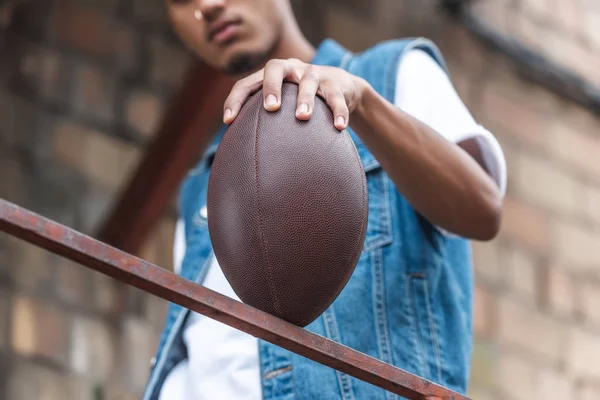 Selective focus of american football ball in hand of young man at street — Stock Photo