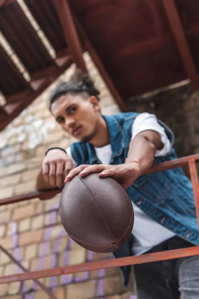 Selective focus of mixed race man showing rugby ball at urban street — Stock Photo