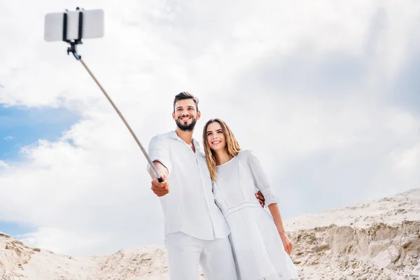 Happy young couple taking selfie with monopod and smartphone in desert — Stock Photo