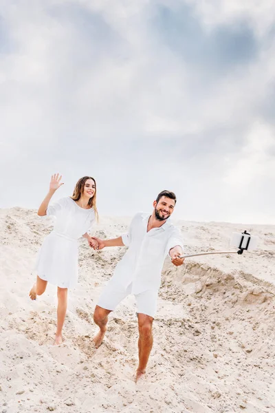 Giocoso giovane coppia scattare selfie con monopiede e smartphone nel deserto — Foto stock