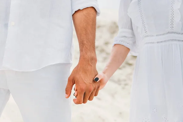Plan recadré de couple en blanc tenant la main devant une dune sablonneuse — Photo de stock