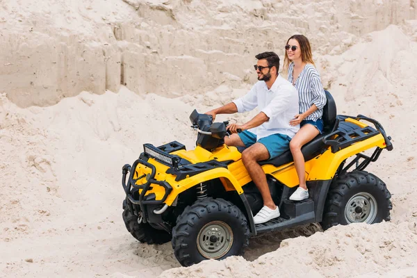 Hermosa pareja joven cabalgando vehículo todo terreno amarillo en el desierto - foto de stock