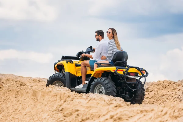 Jovem casal ativo montando veículo todo-terreno no deserto em dia nublado — Fotografia de Stock