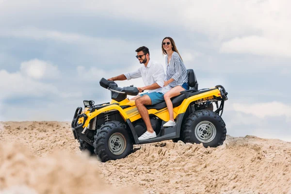 Feliz joven pareja montando todo terreno vehículo en el desierto en día nublado - foto de stock