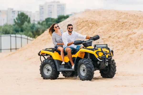 Happy active young couple riding all-terrain vehicle in desert — Stock Photo