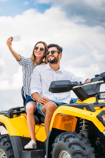 Sorrindo jovem casal tomando selfie enquanto sentado em ATV — Fotografia de Stock