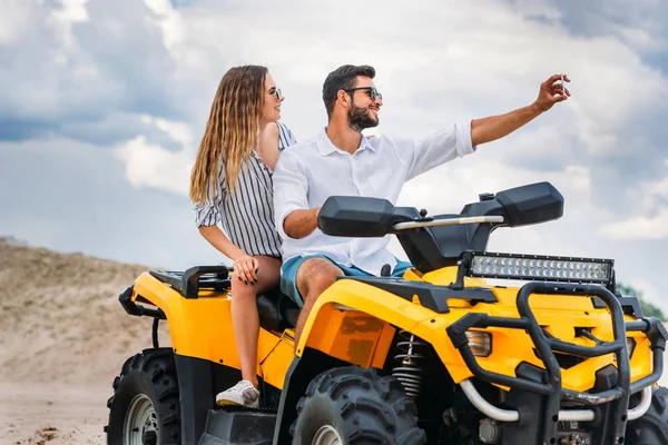 Joven pareja activa tomando selfie mientras está sentado en ATV en el desierto - foto de stock