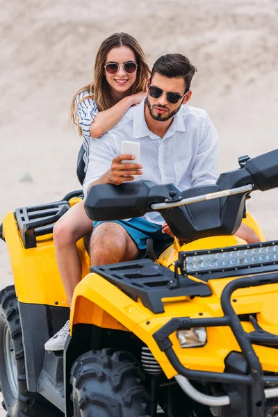 Hermosa joven pareja tomando selfie mientras sentado en ATV en desierto - foto de stock