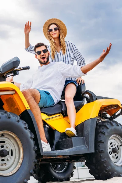 Happy young couple sitting on ATV in front of cloudy sky and looking at camera — Stock Photo