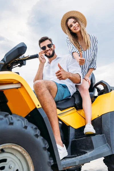 Glückliches junges Paar sitzt auf atv und zeigt Daumen nach oben — Stockfoto