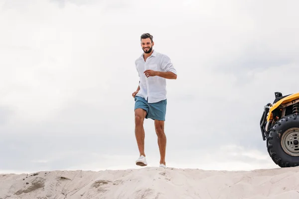 Jovem atraente correndo na duna de areia na frente do céu nublado — Fotografia de Stock