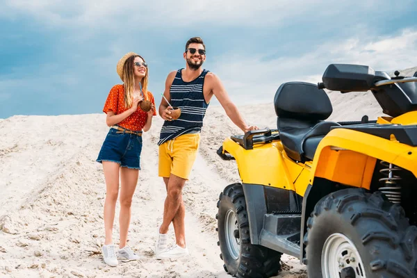 Belo jovem casal com atv e cocos de coco no deserto no dia nublado — Fotografia de Stock