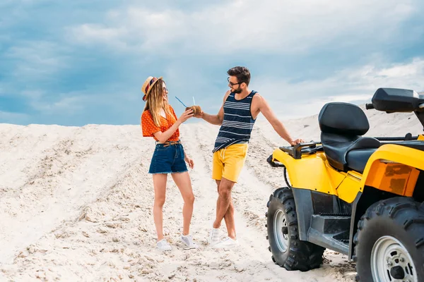 Relaxado jovem casal com ATV e coquetéis de coco no deserto — Fotografia de Stock