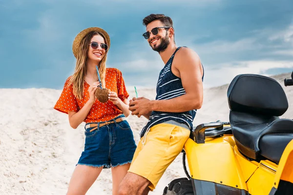 Happy young couple with atv and coconut cocktails in desert — Stock Photo