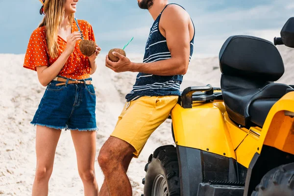 Corte tiro de jovem casal com atv e cocos de coco no deserto — Fotografia de Stock