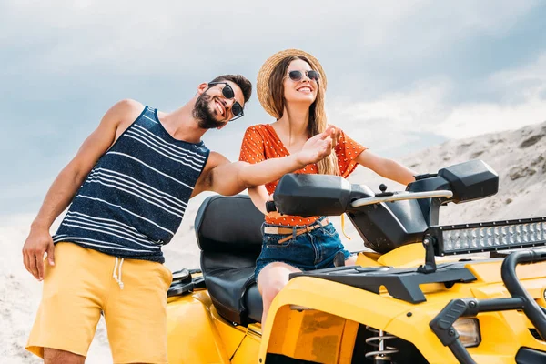 Smiling young man teaching his girlfriend how to ride atv in desert — Stock Photo
