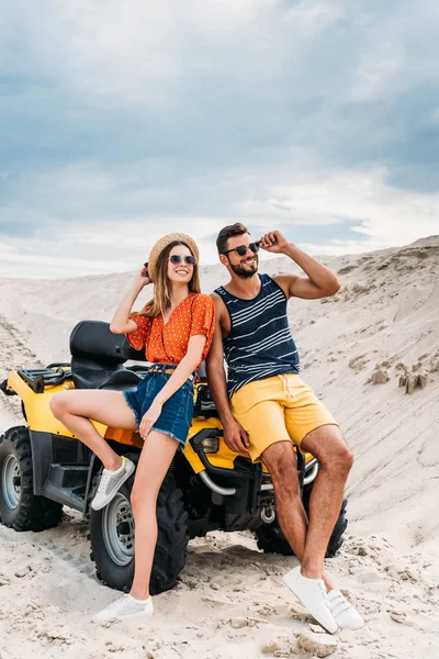 Elegante pareja joven apoyada en ATV en el desierto - foto de stock