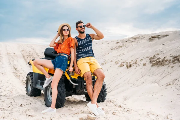 Feliz joven pareja apoyándose en ATV en el desierto - foto de stock