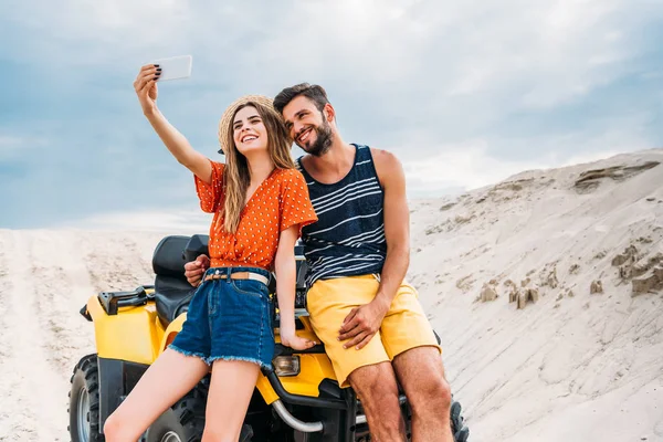 Feliz joven pareja con ATV tomando selfie en el desierto - foto de stock